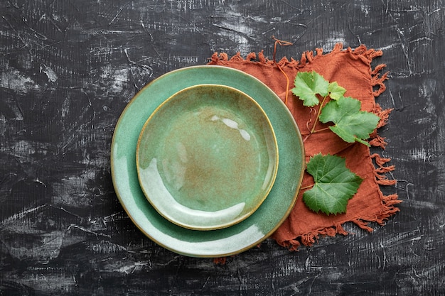 Empty green plate served with grape leaf plant table napkin. Mockup template plate for luxury dinner in wine restaurant with Mediterranean cuisine. Dark black concrete table or chalk board.