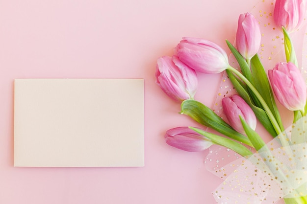 Empty greeting card and pink tulips bouquet on pink background flat lay 8 march Happy Mothers day