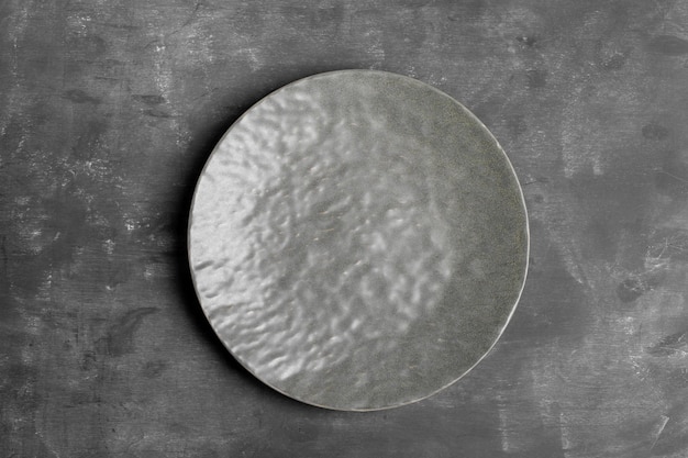 Empty grey textured plate in center of dark grey background Mock up for prepared dish recipe or text Monochrome minimal image Top view Copy space Horizontal orientation