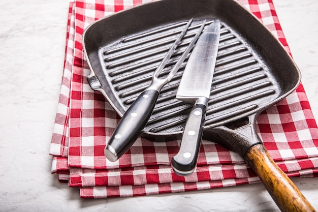 Empty grill pan on marble table with red tablecloth knife and fork.