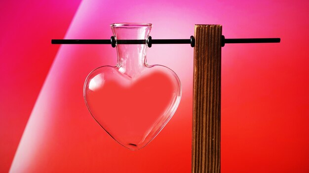 Empty heart shaped glass jar on wooden stand on red. Valentines day vase