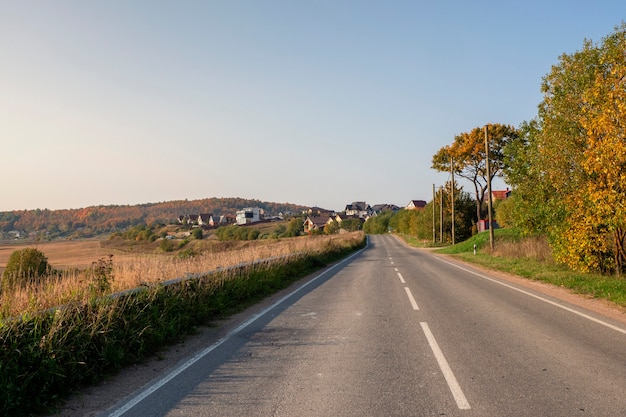 An empty highway country road among beautiful autumn hills with cottages.