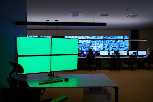 Empty interior of big modern security system control room with blank green screens, workstation with multiple displays, monitoring room with at security data center  Empty office, desk, and chairs at