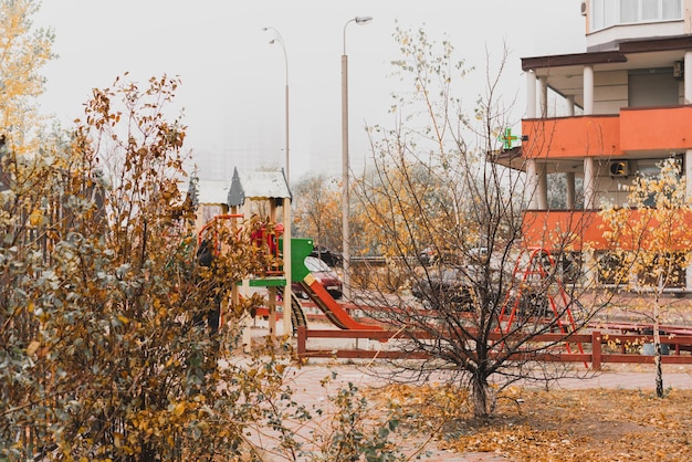 Empty kids playground near building and trees at autumn. Weather. Cold. Outdoor. Cheap. No people. Slide. Depressive. Depression