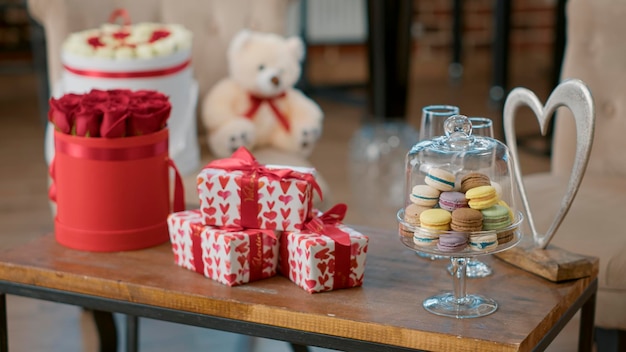 Soggiorno vuoto con nessuno dentro che ha un tavolo con regalo di san valentino e rose rosse su di esso decorato dal fidanzato per celebrare il giorno di san valentino a casa con la fidanzata. concetto di anniversario d'amore