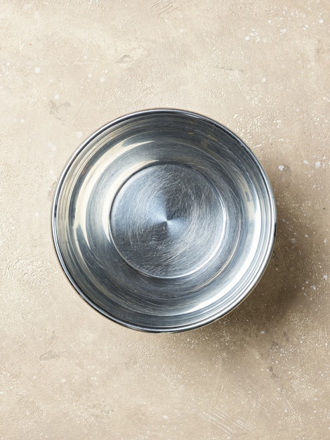 Empty metal bowl on a beige color kitchen table, top view