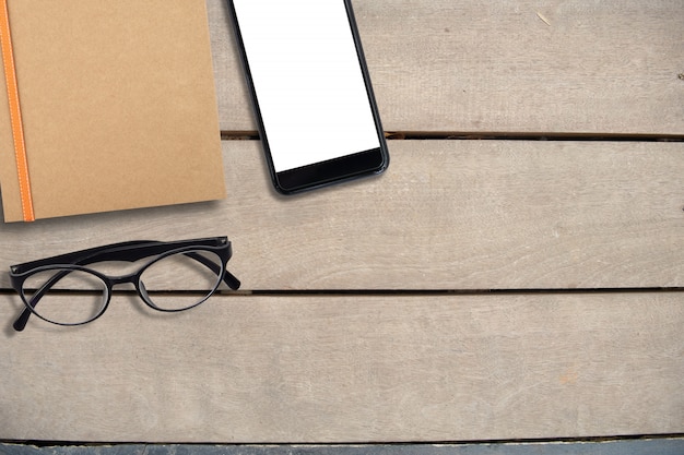 Empty mobile screen and book of brown and eye glasses on desk, top view, copy space, business and freelance background concept
