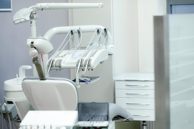 Пустое современное стоматологическое кресло и электрические инструменты стоматолога, полировщик, дрель, турбина, наконечник, включенный в основной блок рядом с плевательницей в кабинете стоматолога. Стоматология, медицинское оборудование, концепция стоматологической помощи.