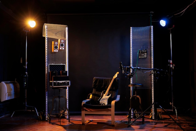 Empty music recording studio with guitar on chair, next to amps, sound amplifier equipment. Nobody in professional dark rock room, performance speaker
