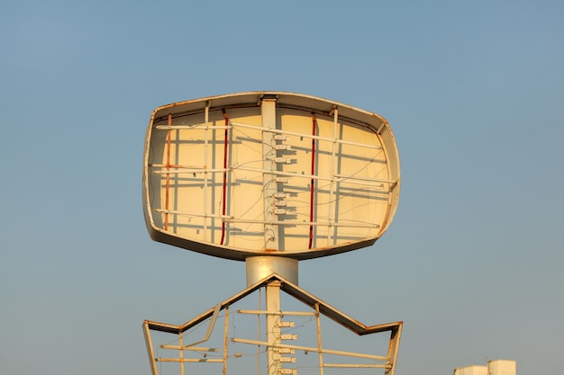 Empty neon advertising sign, tubes visible, clear afternoon sky in background.