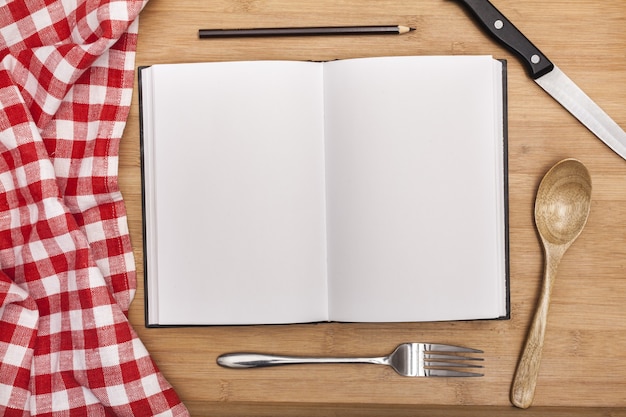 Empty notebook for recipes with utensils and tablecloth on wooden table