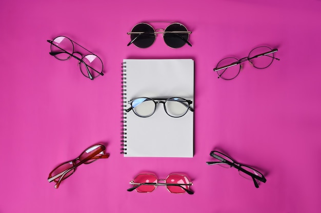 Empty notebook and sunglasses on pink background.