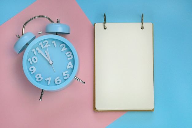 Empty notebook with a blue alarm clock on a paper combined background 