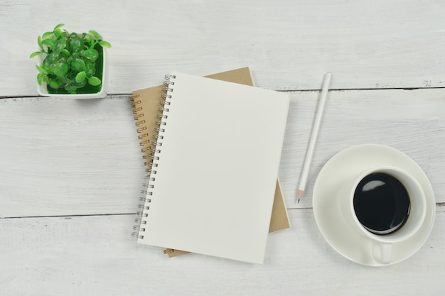 Empty notebook with cup of coffee, eyeglasses and pencil on white wooden table.