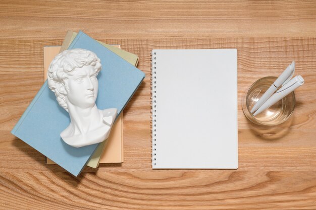 Empty notebook on wooden table with books and small David plaster sculpture