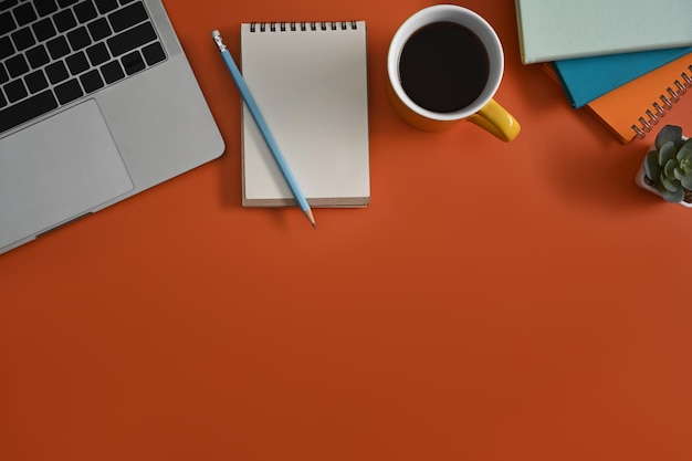 Empty notepad laptop computer and coffee cup on orange background Top view