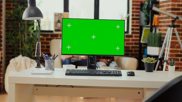 Empty office desk with greenscreen display on computer used to work on freelance in living room workspace. Monitor showing isolated chroma key and blank mockup copyspace on screen.