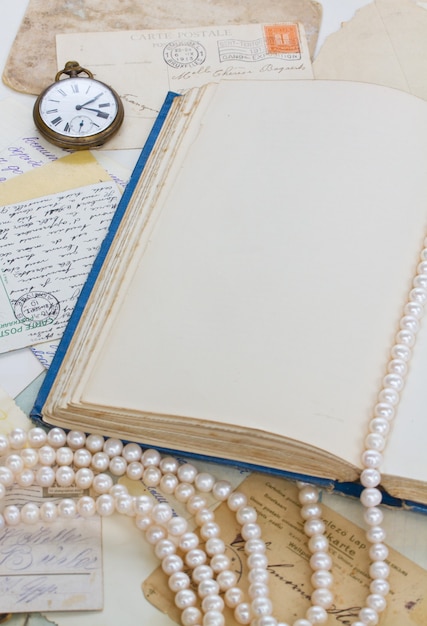 Empty old book page with  antique postcards and strand of pearls vintage background with copy space