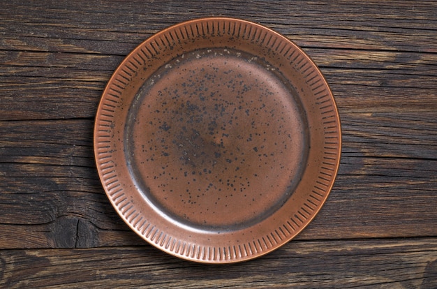 Empty old brown plate on dark wooden table, top view