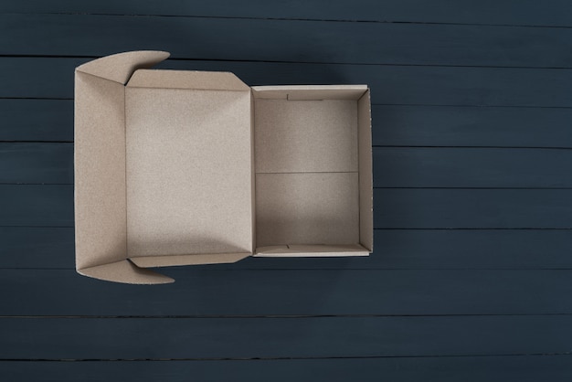 Empty open cardboard box on black wooden background