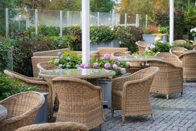 Empty outdoor cafe terrace with wicker furniture and growing\
flowers in pot for summer entertainment