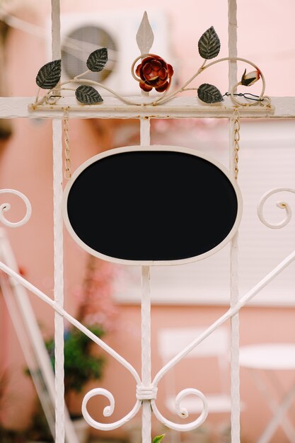 Photo empty oval sign on the surface of a beautiful forged white fence with flowers