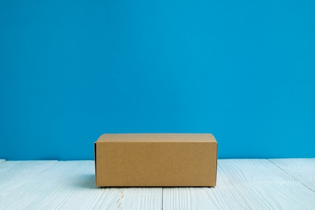 Empty Package brown cardboard box or tray on bright white wooden table with blue wall background.