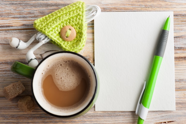 Empty paper note, green pen, earphones and mug of coffee