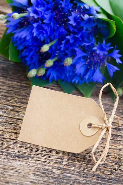 Empty paper tag with Blue fresh cornflowers on wooden table  