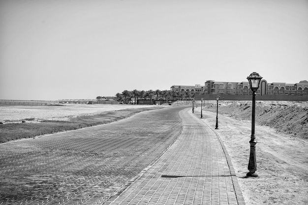 Empty paved public walkway pedestrian walk pavement or sidewalk along sea or ocean shore coast beach at hotel resort on sunny summer day on clear blue sky background Vacation and leisure