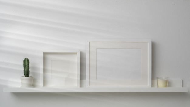 Empty photo frames and decorations on white shelf with white wall