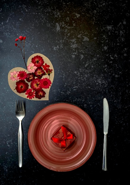 Пустая розовая тарелка с подарочной вилкой и ножом Сердце, полное красных цветов Концепция Дня святого Валентина