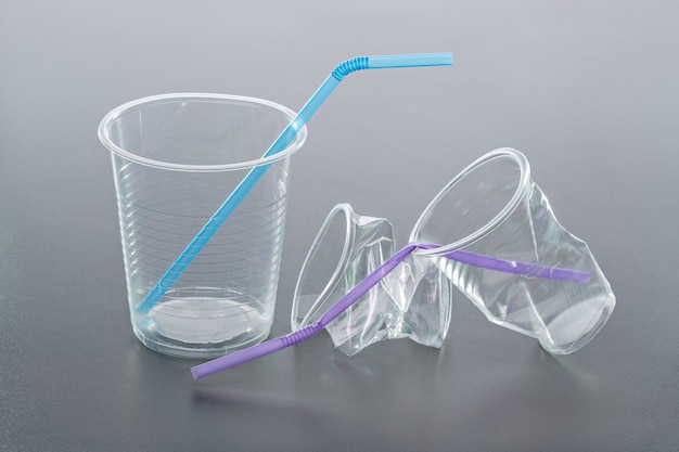 Foto bicchiere di plastica vuoto con paglia. bicchieri di plastica e paglia, sfondo grigio.