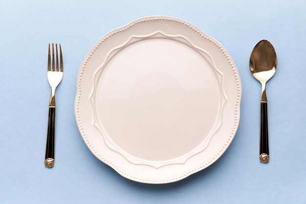 Фото Пустая тарелка и вилка с ложкой на синем фоне