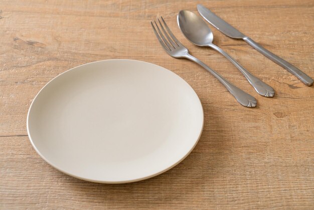 Empty plate or dish with knife fork and spoon on wood tile background