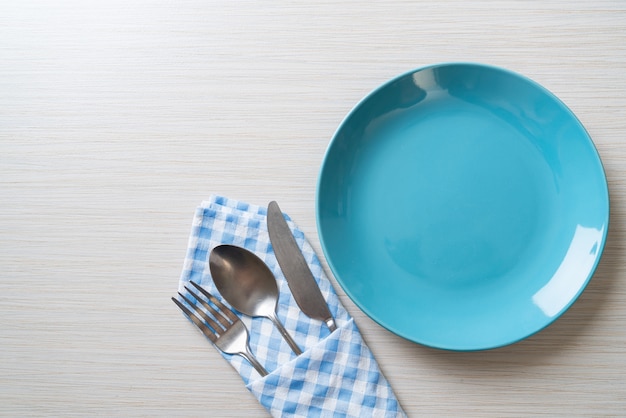 пустая тарелка или блюдо с ножом, вилкой и ложкой на деревянной плитке