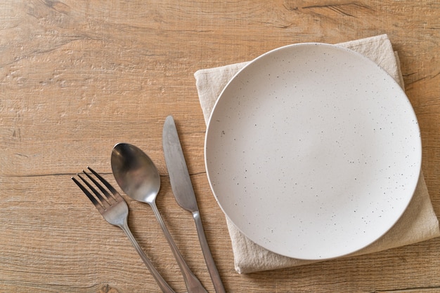 empty plate or dish with knife, fork and spoon on wooden table