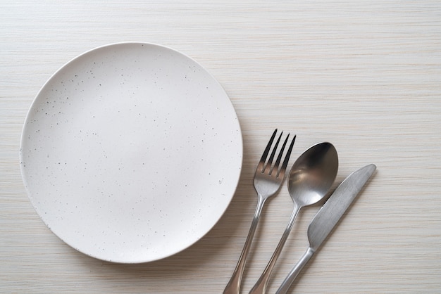 пустая тарелка или блюдо с ножом, вилкой и ложкой на деревянном столе