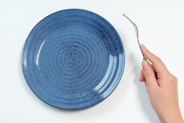 Empty plate and female hand with fork on white background closeup top view