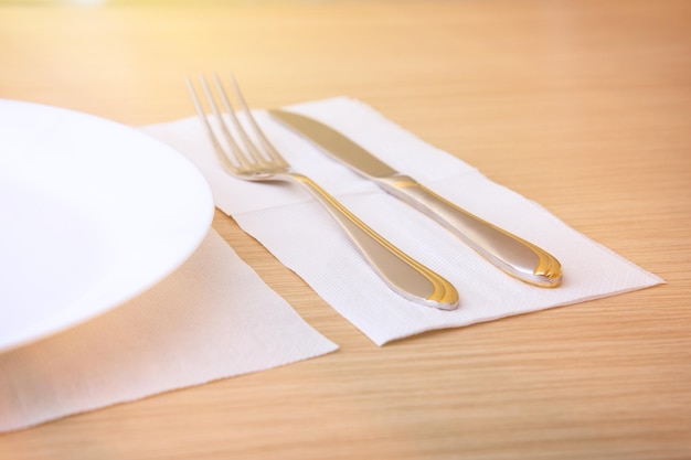 An empty plate, fork, knife, on a wooden table, side view.