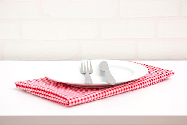Пустая тарелка на красной скатерти над столом с кирпичными обоями