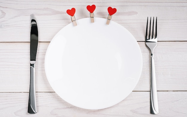Пустая тарелка на белом деревянном фоне, украшенная сердечками на день святого Валентина