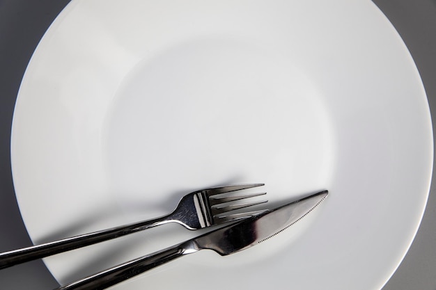 Empty plate with fork and knife on gray background top view for copy space food and healthy eating