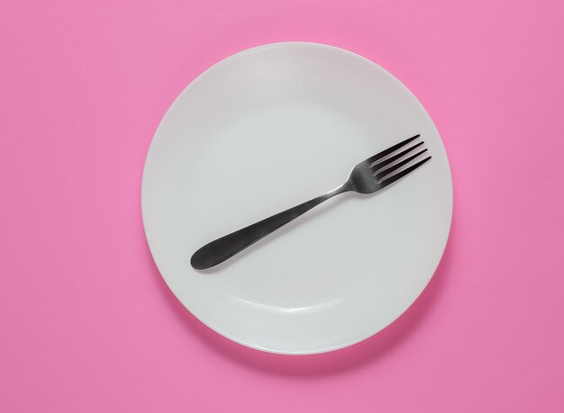 Empty plate with a fork on pink background. Studio shot. Restaurant food concept.