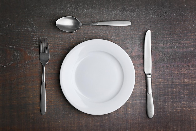 Empty plate with silver cutlery on background