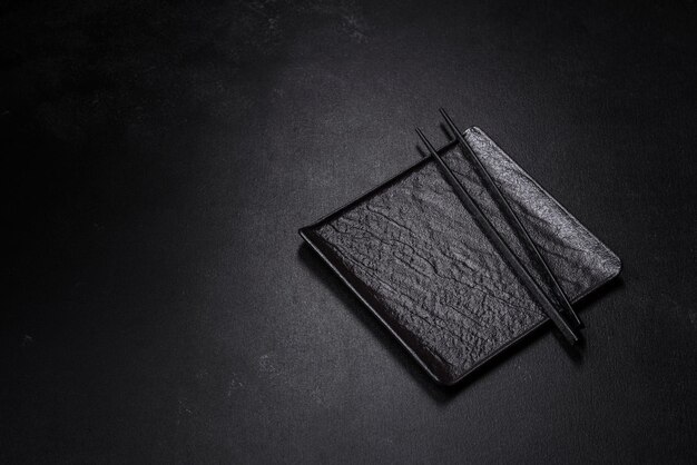 Empty plate with wooden sticks for Asian food on a dark concrete background