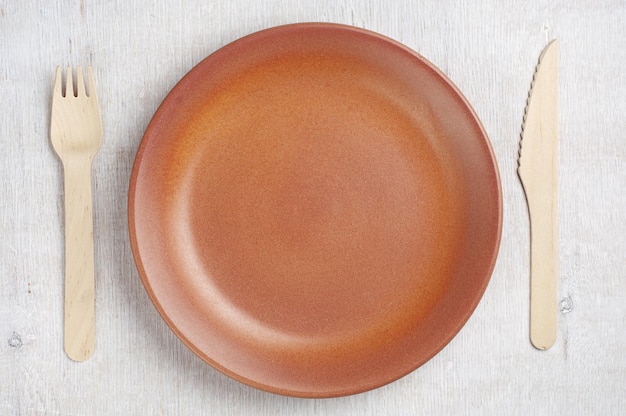 Empty plate, wooden fork and table knife on rustic table, top view