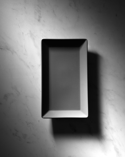 Пустая прямоугольная черная тарелка с отражением теней на сером мраморном фоне с копией пространства. Вид сверху