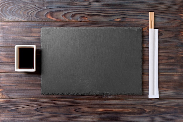 Empty rectangular black slate plate with chopsticks for sushi and soy sauce on wood