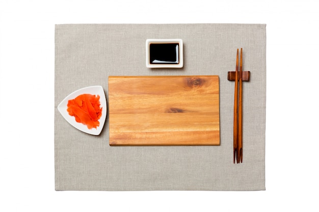 Empty rectangular brown wooden plate with chopsticks for sushi, ginger and soy sauce on grey napkin . Top view with  copyspace 